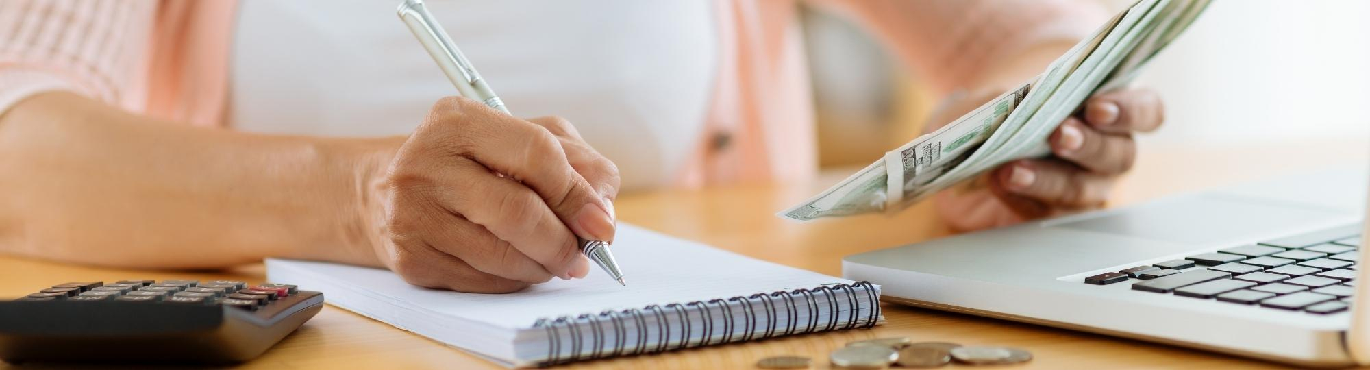 Woman writing in notebook while holding money