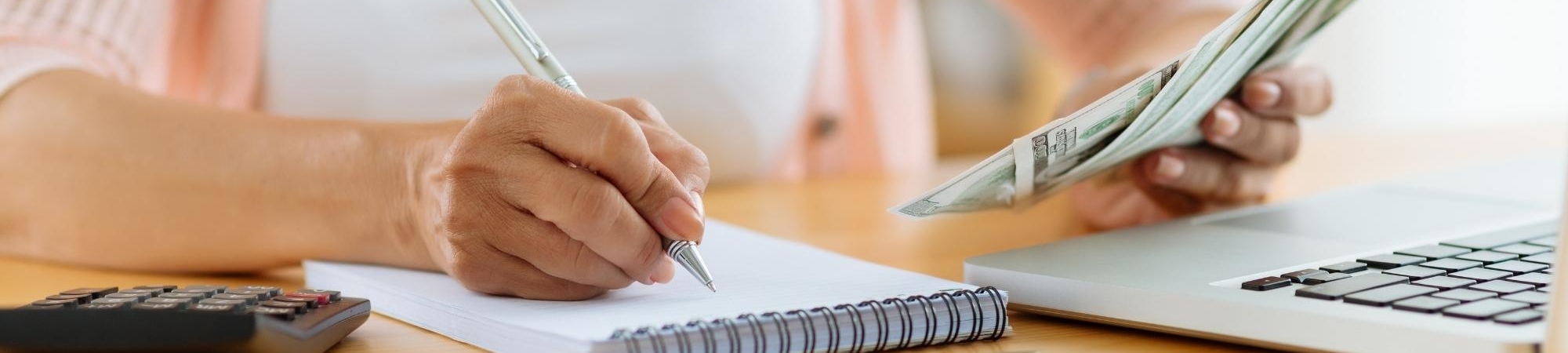 Woman writing in notebook while holding money